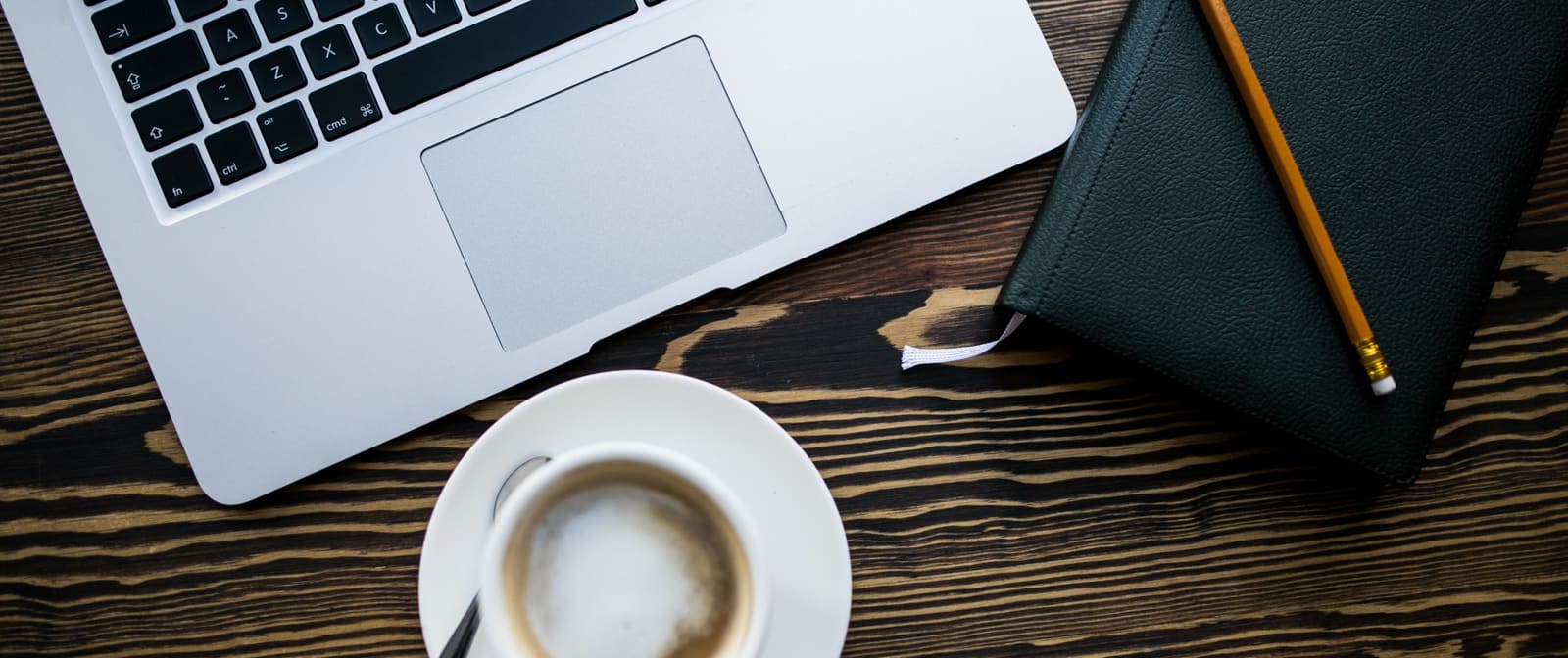 A laptop, notebook and coffee on a wooden desk